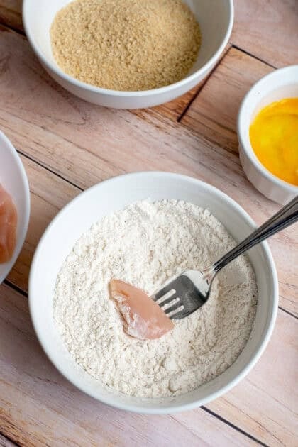 Coating a piece of chicken with flour.