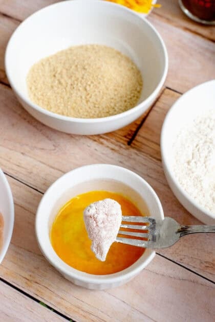 Dunking a piece of chicken in egg yolk.