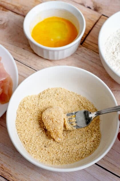 Coating a piece of chicken in breadcrumbs.