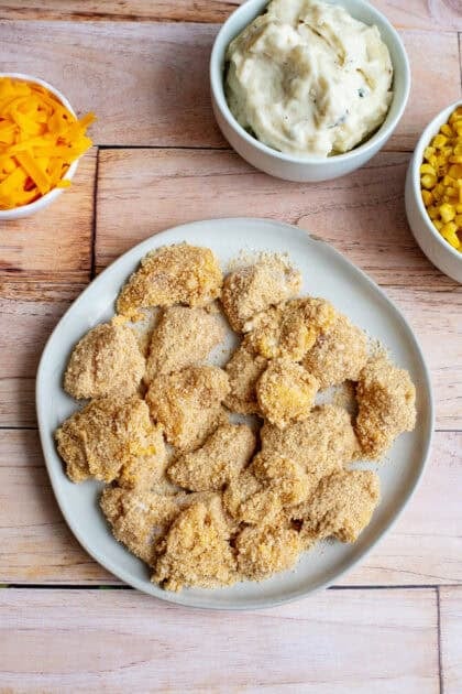 Breaded chicken nuggets in a plate over a wooden surface, ready for frying.