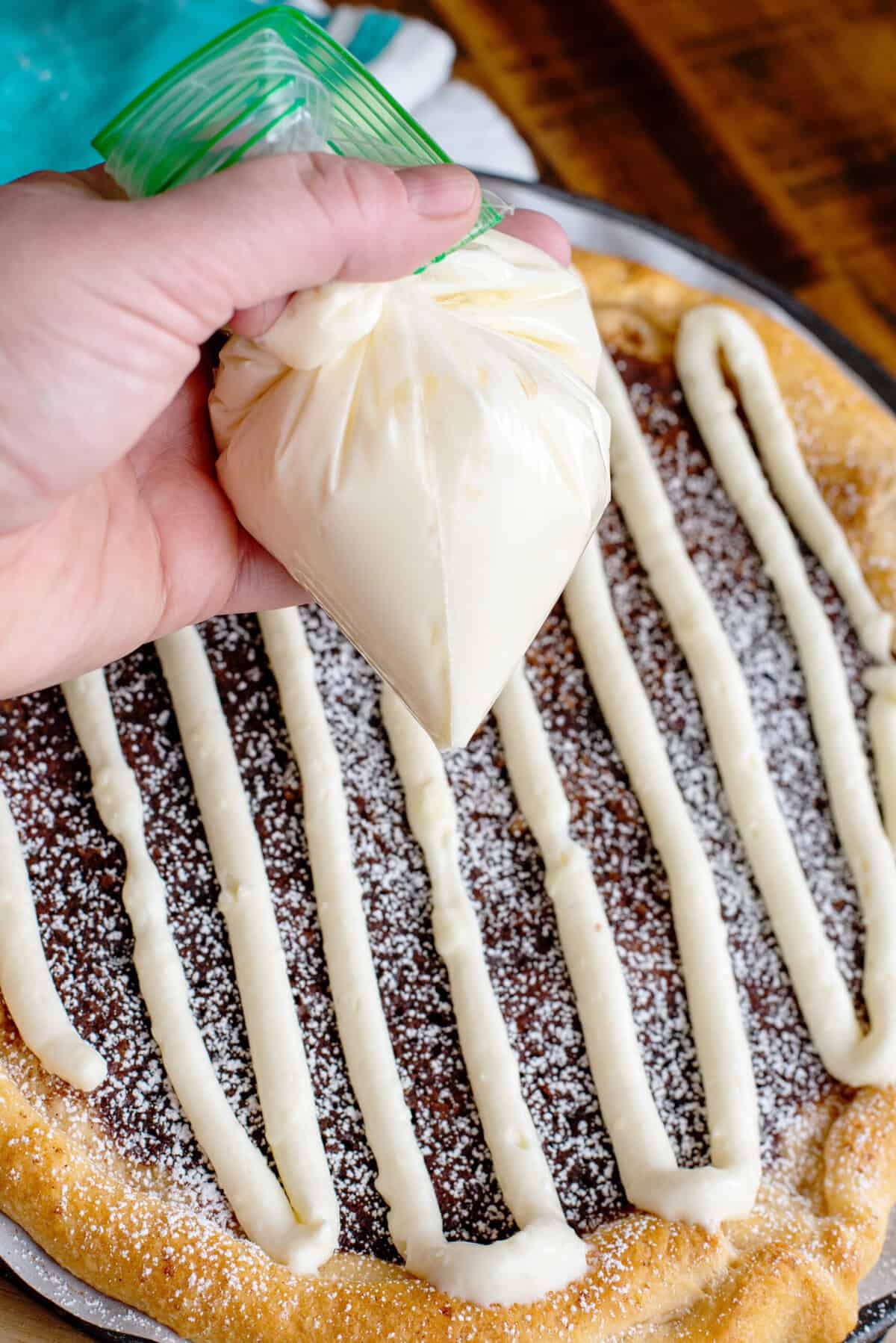 Piping on the cream cheese glaze for cinnamon sugar dessert pizza.