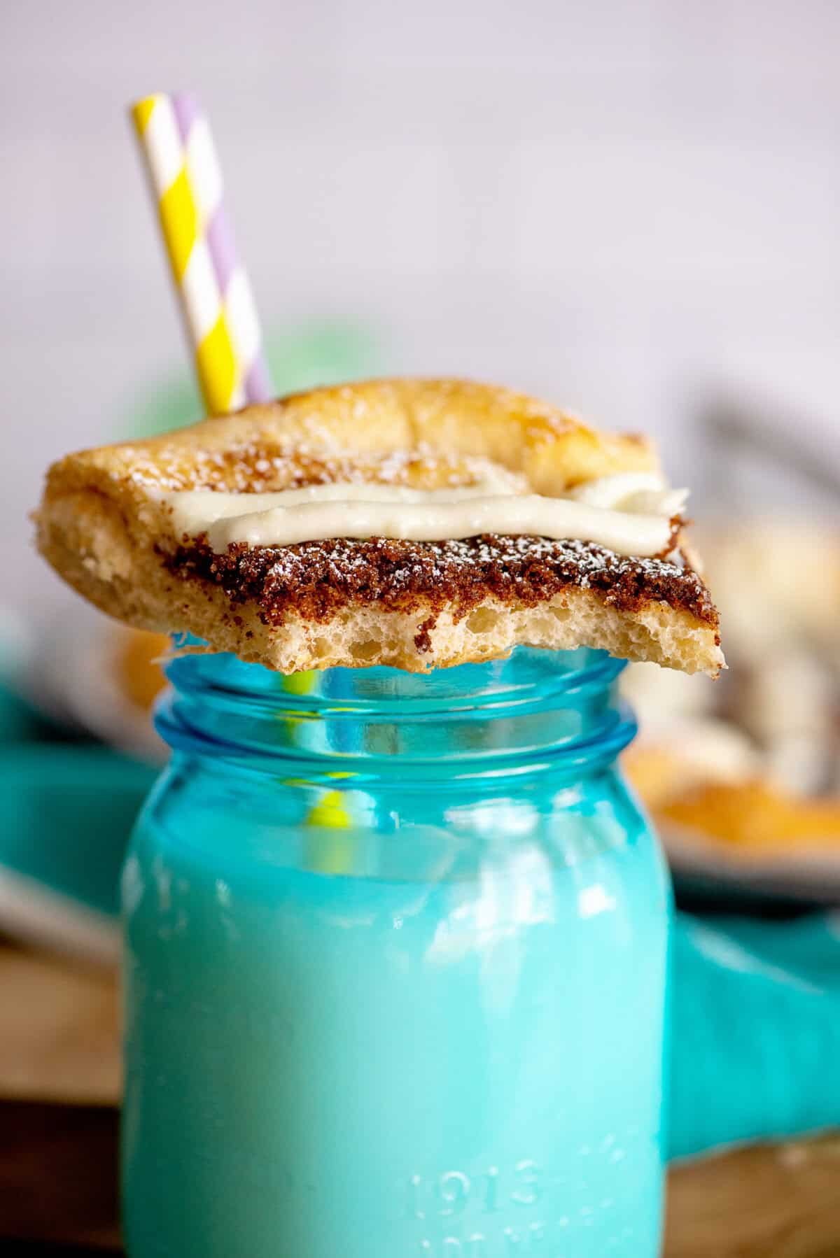 A slice of cinnamon sugar dessert pizza resting on a turquoise mason jar of milk.