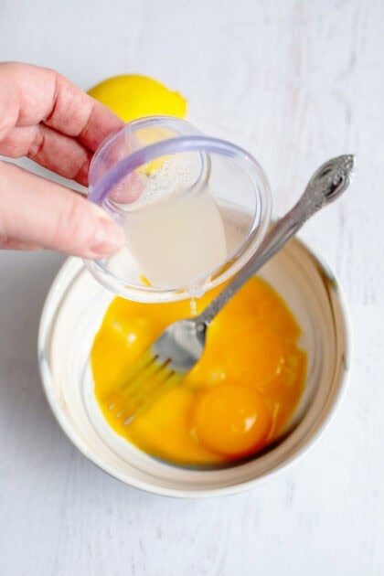 Pouring lemon juice into a bowl of egg yolks