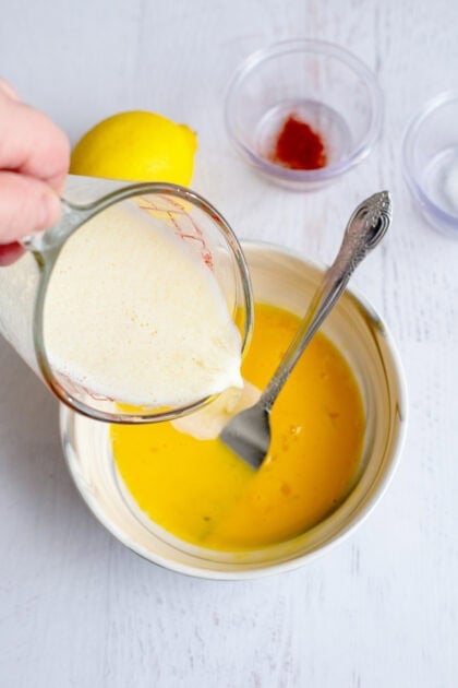 Pouring melted butter into a bowl of whisked egg yolks