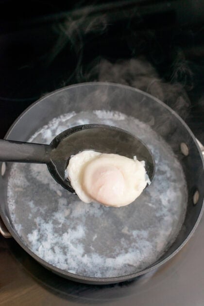 Removing a cooked egg from hot simmering water