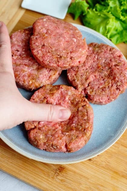 Person making shallow depression in the center of raw patties