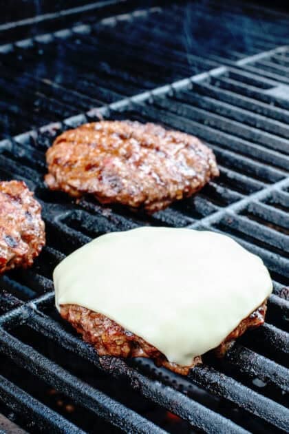 Burger patty on the grill with melted cheese on top