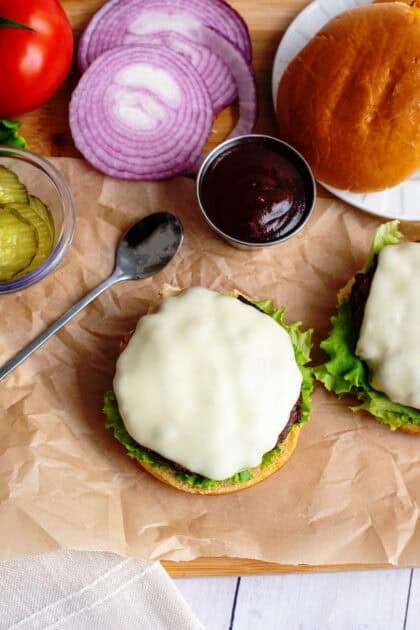 Burger with melted cheese on burger bun next to other toppings