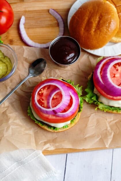 Red onions on burger that is being assembled, next to other toppings