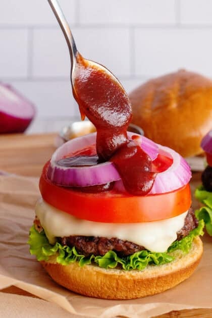 Drizzling barbecue sauce on a burger that is being assembled