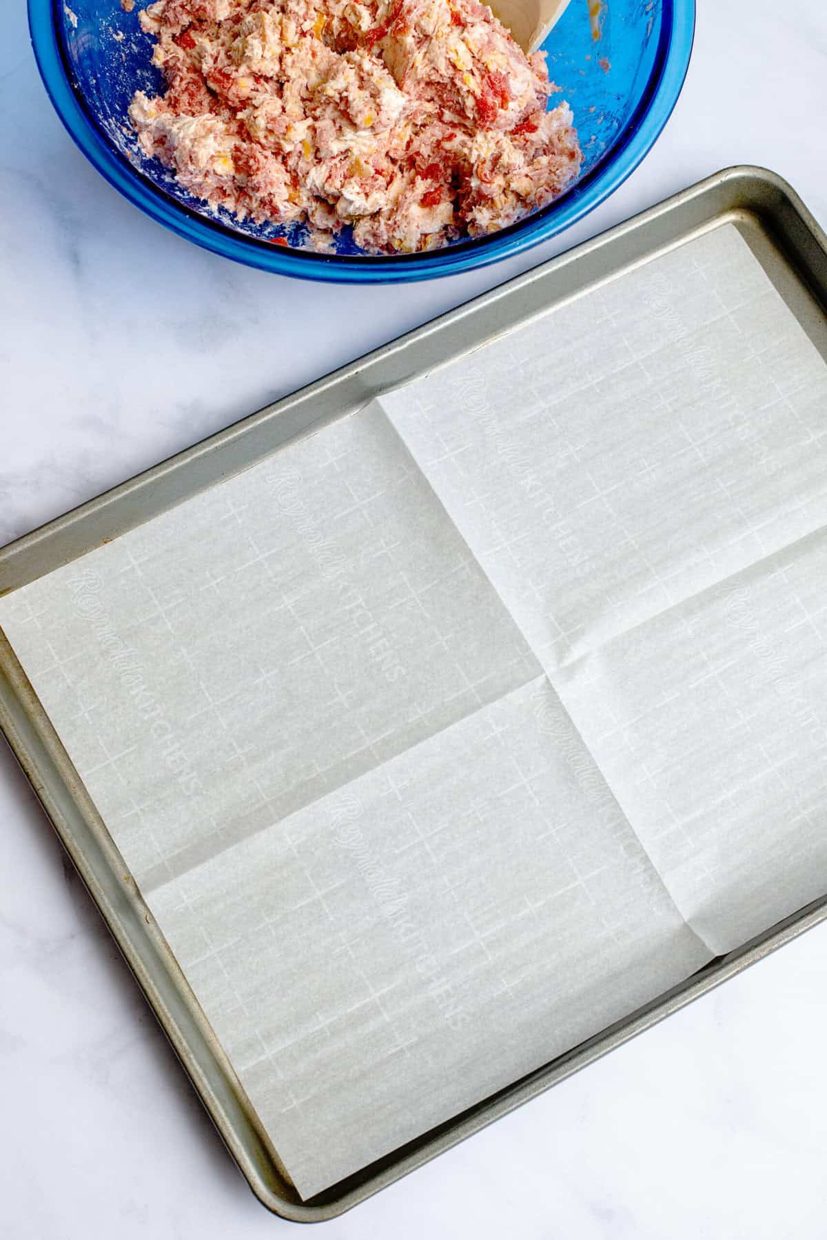 Baking sheet lined with parchment paper next to bowl of Rotel cream cheese sausage ball mixture