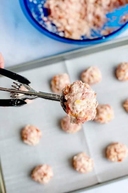 Cream cheese sausage ball mix in cookie scoop over a baking sheet with other sausage balls 