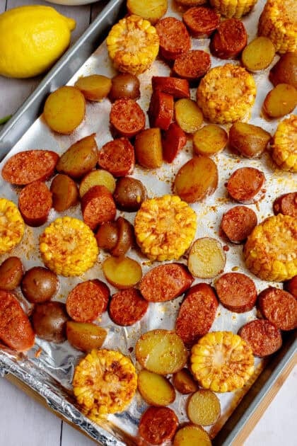 Corn, red potatoes, and sausages spread on large baking sheet