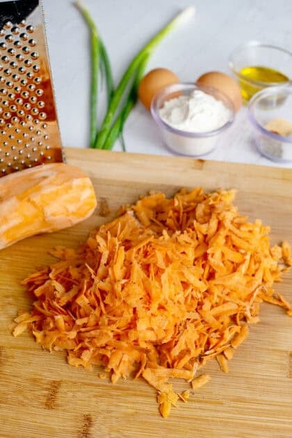 Grated sweet potatoes on a cutting board next to a hand grater