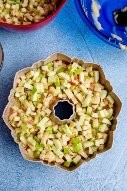 A layer of chopped apples over a bed of the apple pound cake mixture in a bundt pan