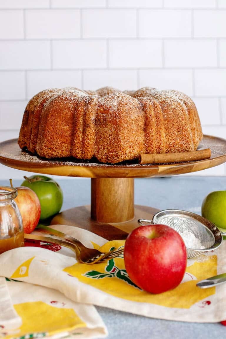 Rustic apple pound cake on a serving tray with apples under it
