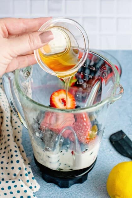 Adding honey to a blender filled with berries