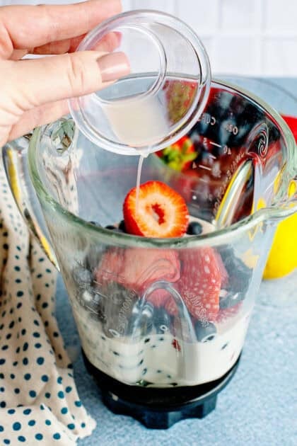 Adding coffee creamer into a blender filled with berries