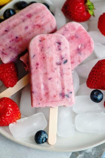 Berries and cream popsicles on a plate with ice and berries