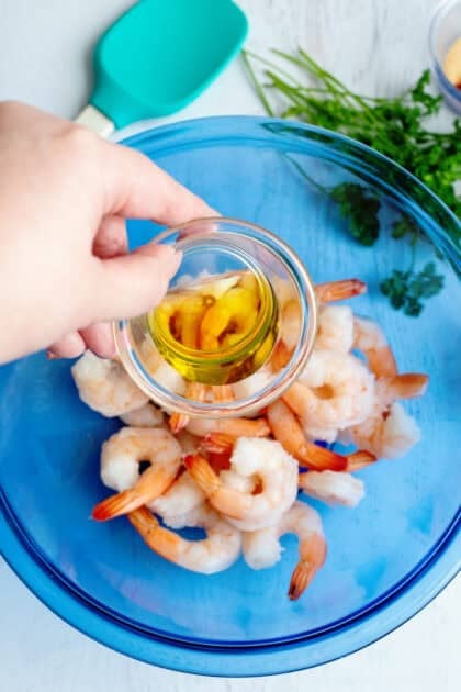 Adding olive oil to a bowl of raw shrimp