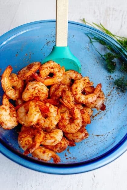 Tossing raw shrimp in olive oil, cajun seasoning, garlic powder, and smoked paprika