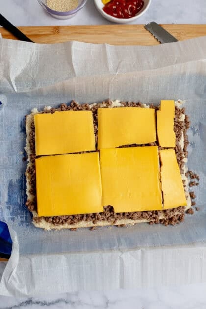 American cheese slices on top of ground beef and bottom rolls