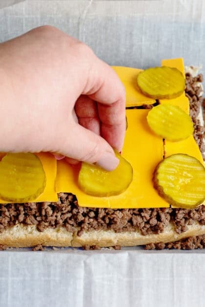Adding pickle slices on top of cheese and ground beef