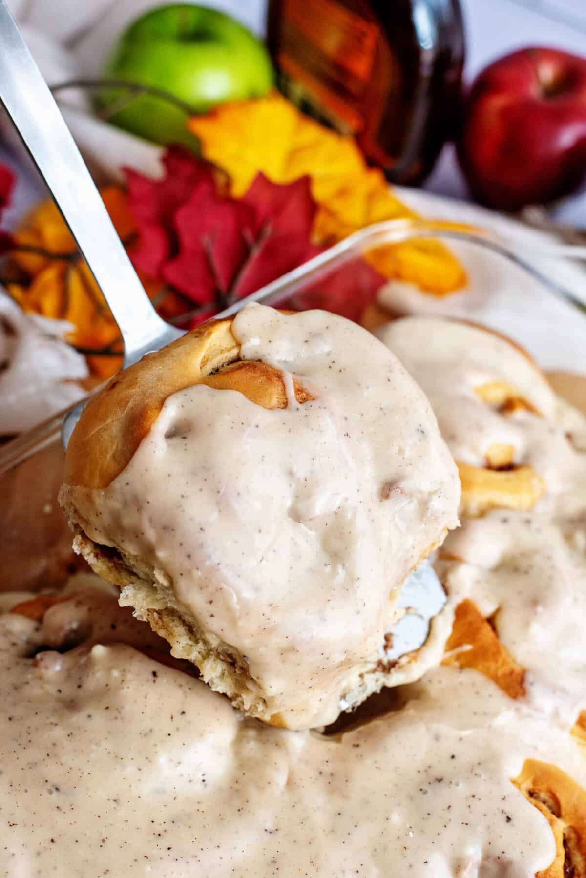 An apple cinnamon roll being taken from baking pan