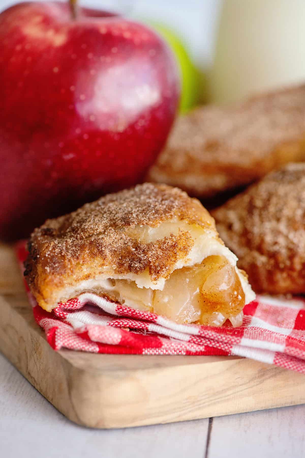 Fried apple hand pie with a bite taken out on a serving board with an apple in the background