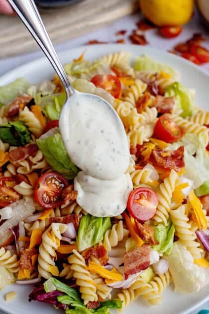 Pouring the dressing over the cooked BLT pasta salad