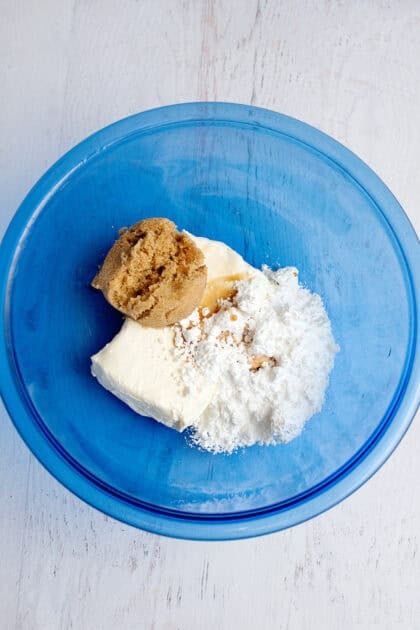 A bowl of ingredients for the cream cheese topping. Softened cream cheese, brown sugar, powdered sugar, and vanilla