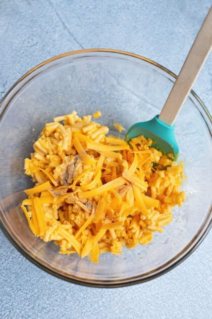 Combining cooled mac and cheese with shredded cheddar, garlic powder, salt, and pepper in a bowl