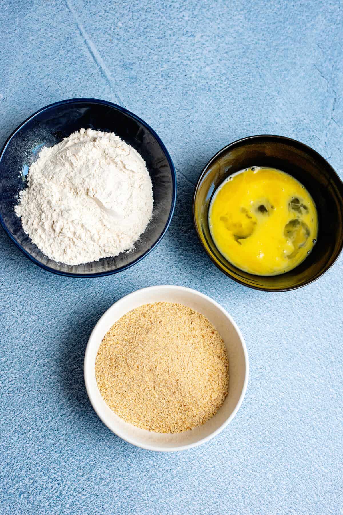 Three bowls with breading ingredients for the mac and cheese balls