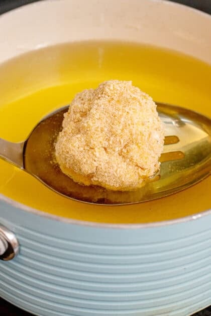 Adding a coated mac and cheese ball to a skillet with oil