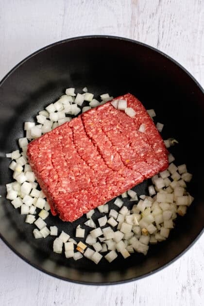 Raw ground beef and raw onions in a skillet