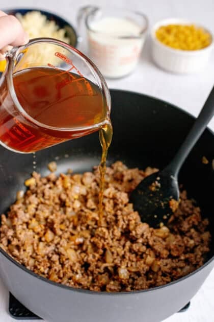 Pouring beef broth into the skillet of cooked hamburger
