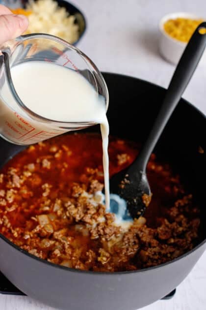 Pouring milk into the skillet of cooked hamburger