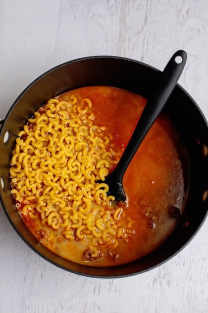Dry pasta in a skillet with cooked hamburger and liquids