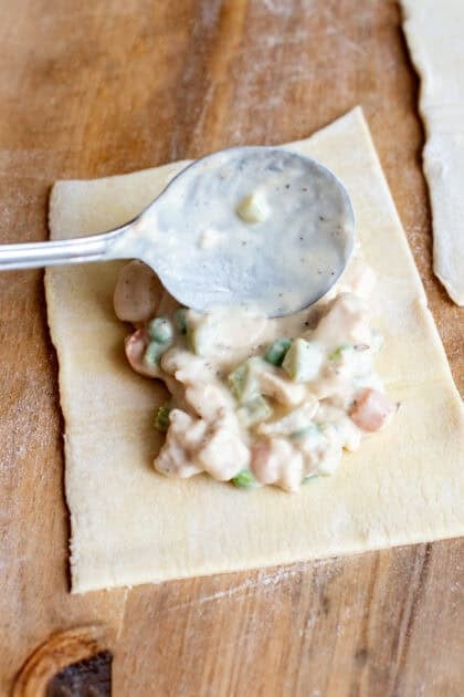 Adding a spoonful of the handheld chicken pot pie mix onto a puff pastry square