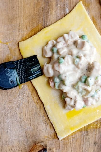 Brushing the edged of a handheld chicken pot pie with egg wash