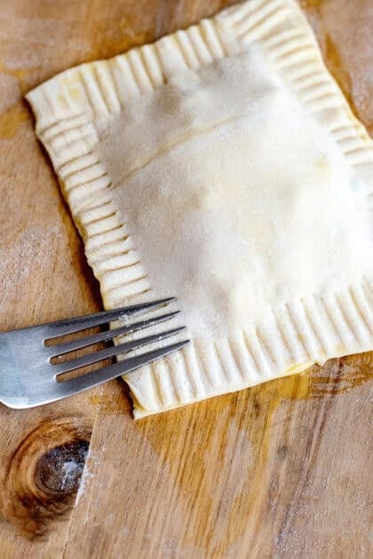 Pressing the edges of a handheld chicken pot pie with a fork