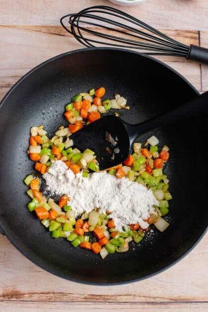 Pouring flour into a large skillet with diced vegetables
