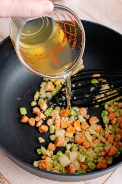 Pouring chicken broth into a skillet with diced vegetables
