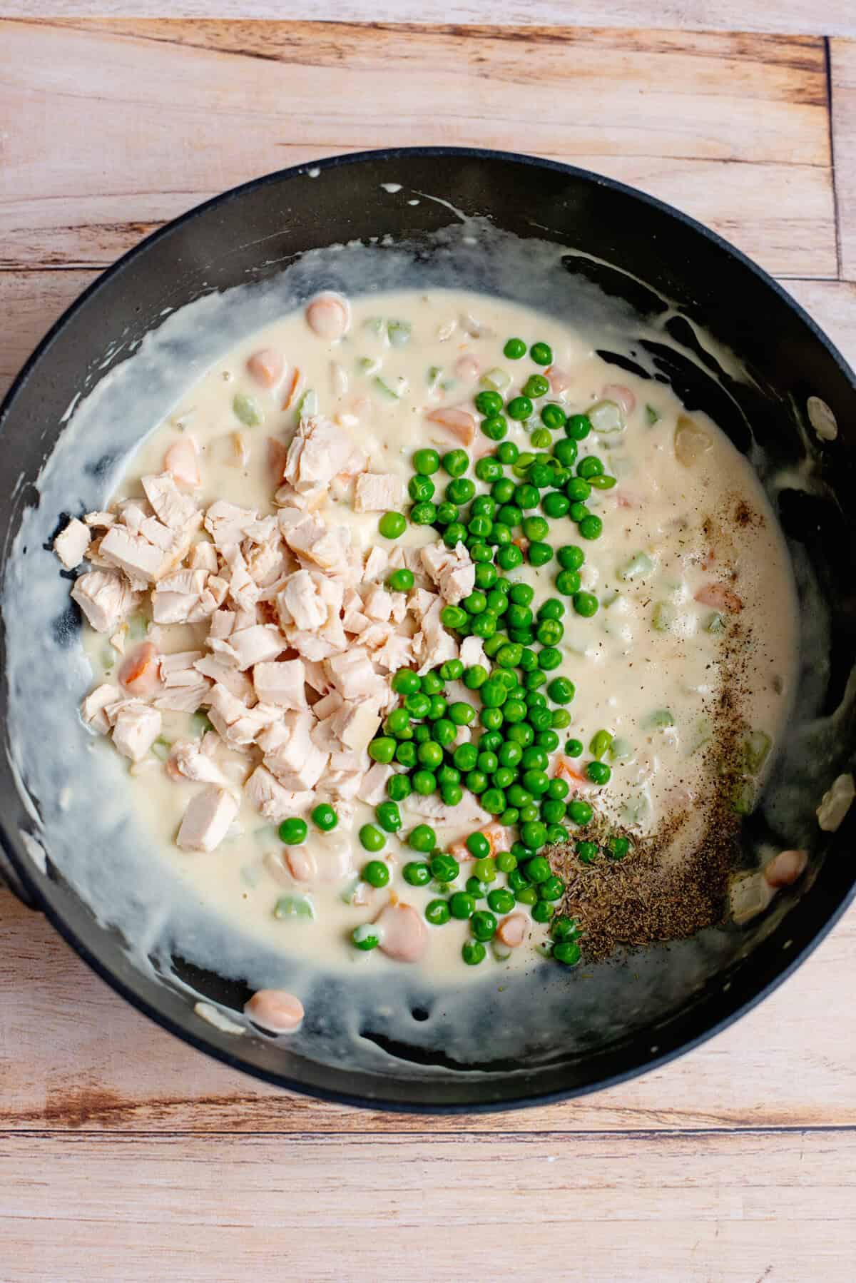Stirring shredded chicken, frozen peas, and seasoning into a large skillet