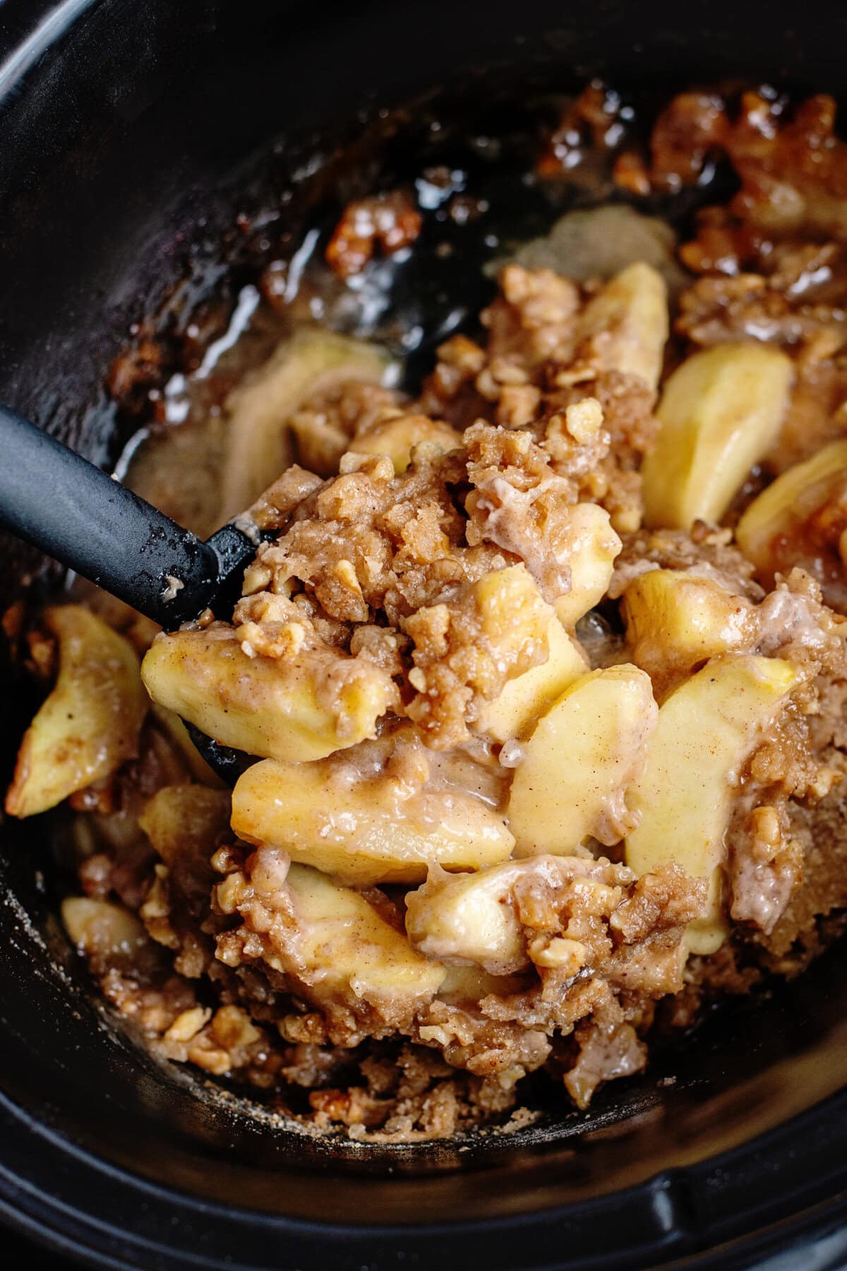 Slow cooker apple crisp being stirred with a spoon
