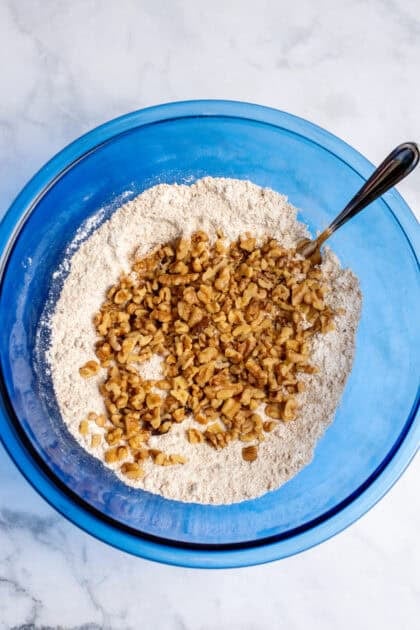 A medium bowl of stirred together dry ingredients for slow cooker apple crisp and chopped walnuts