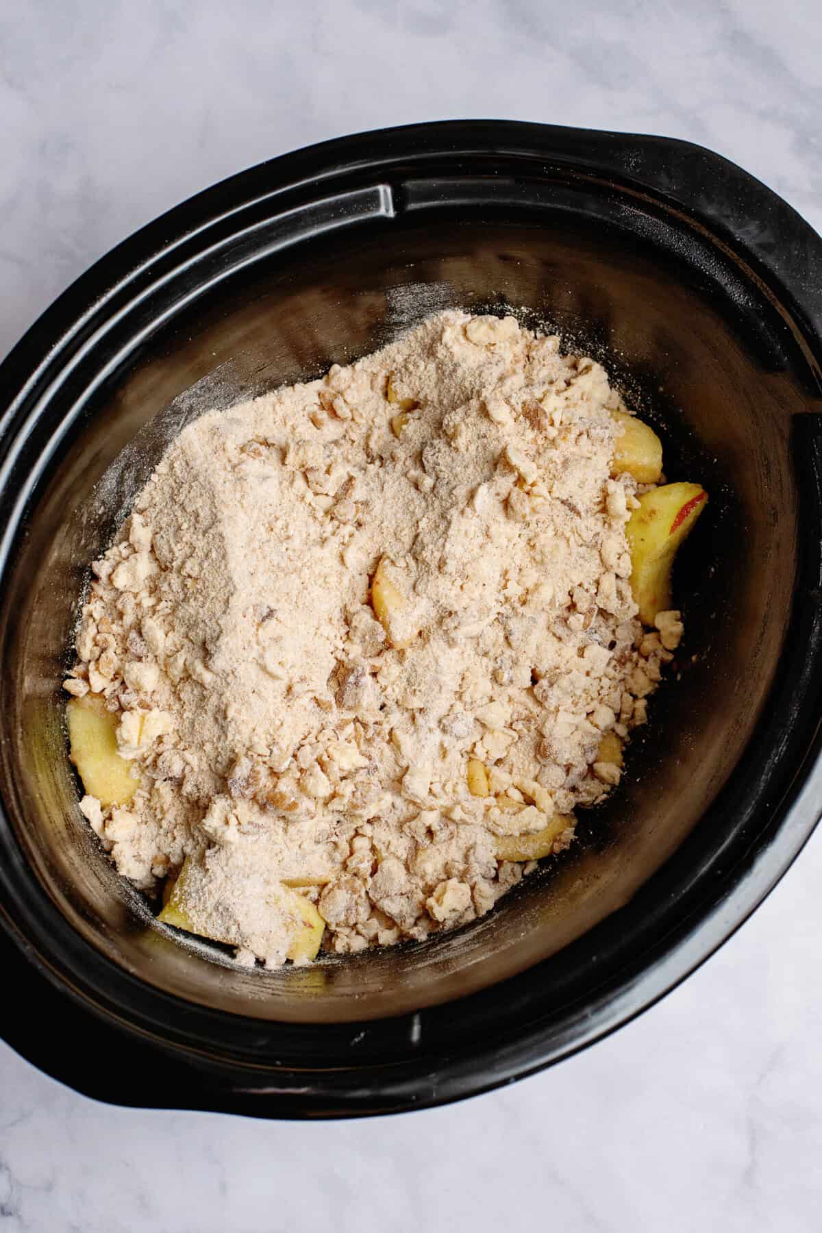 Slow cooker apple crisp mixture poured over apples