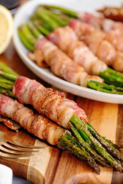 Bacon wrapped asparagus on a wooden cutting board.