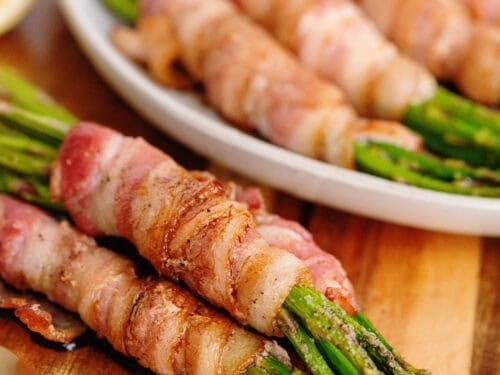 Bacon wrapped asparagus on a wooden cutting board.