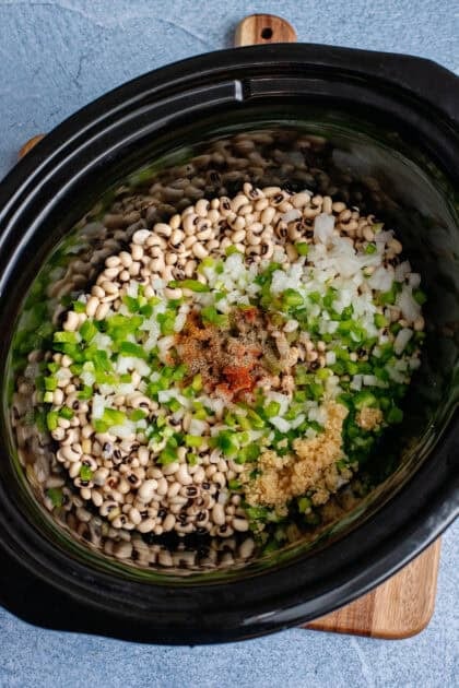 Onion, bell pepper, garlic, and seasonings on a bed of black-eyed peas in the crockpot